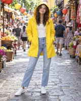 A smiling woman in a yellow hooded raincoat and blue jeans on a busy market street